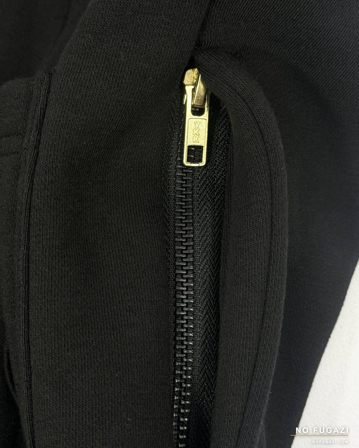 Close-up of a branded metal zip and the topstitching around a black garment pocket
